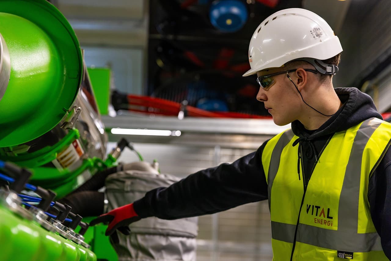 Maintenance technician in safety vest working on green industrial machinery representing mobile maintenance reporting